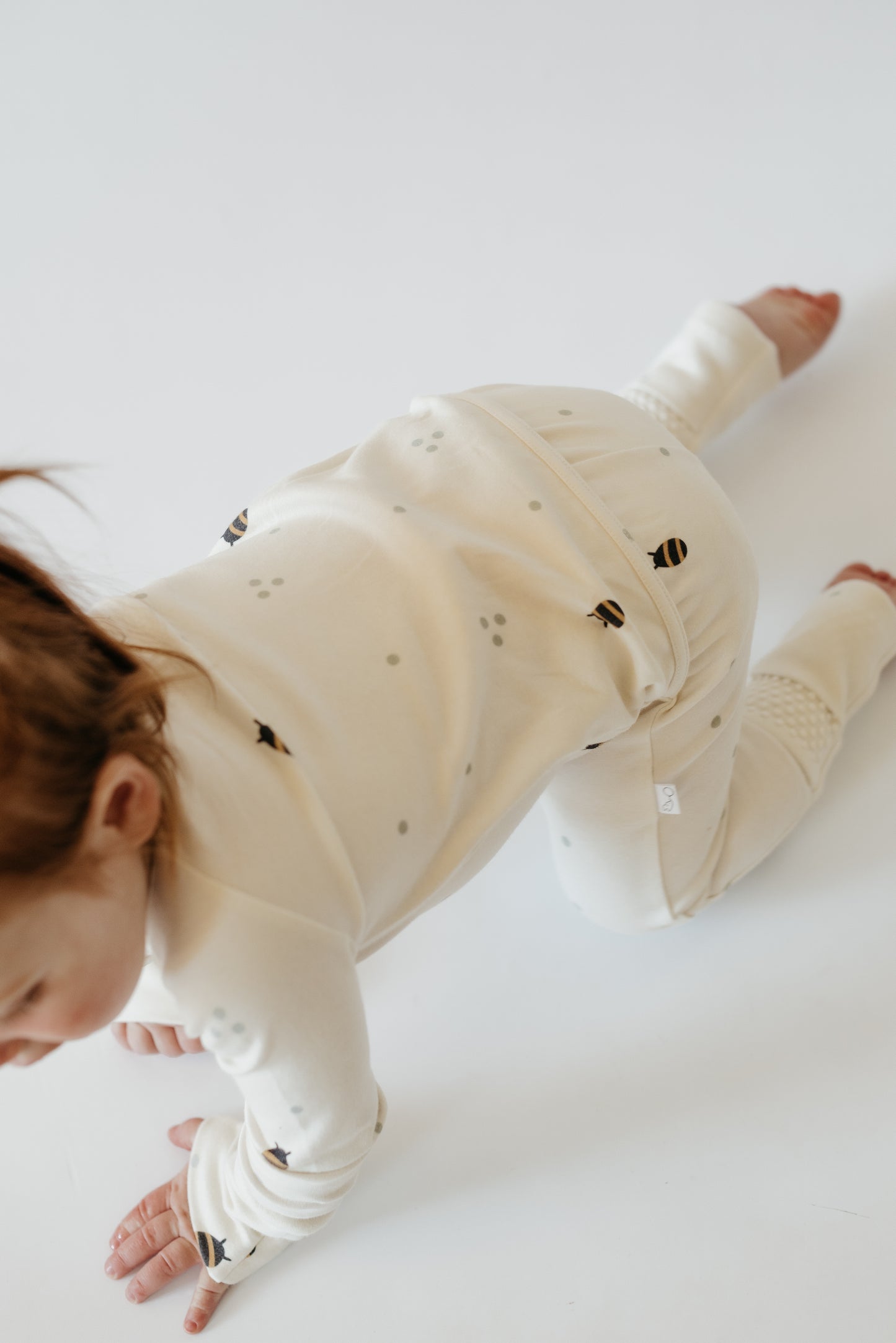 Baby wearing LURE by Lina neutral cotton sleeper — eco-friendly Diaper Peek-a-Boo design with convertible feet and protective zipper flap