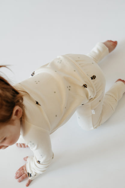 Baby wearing LURE by Lina neutral cotton sleeper — eco-friendly Diaper Peek-a-Boo design with convertible feet and protective zipper flap
