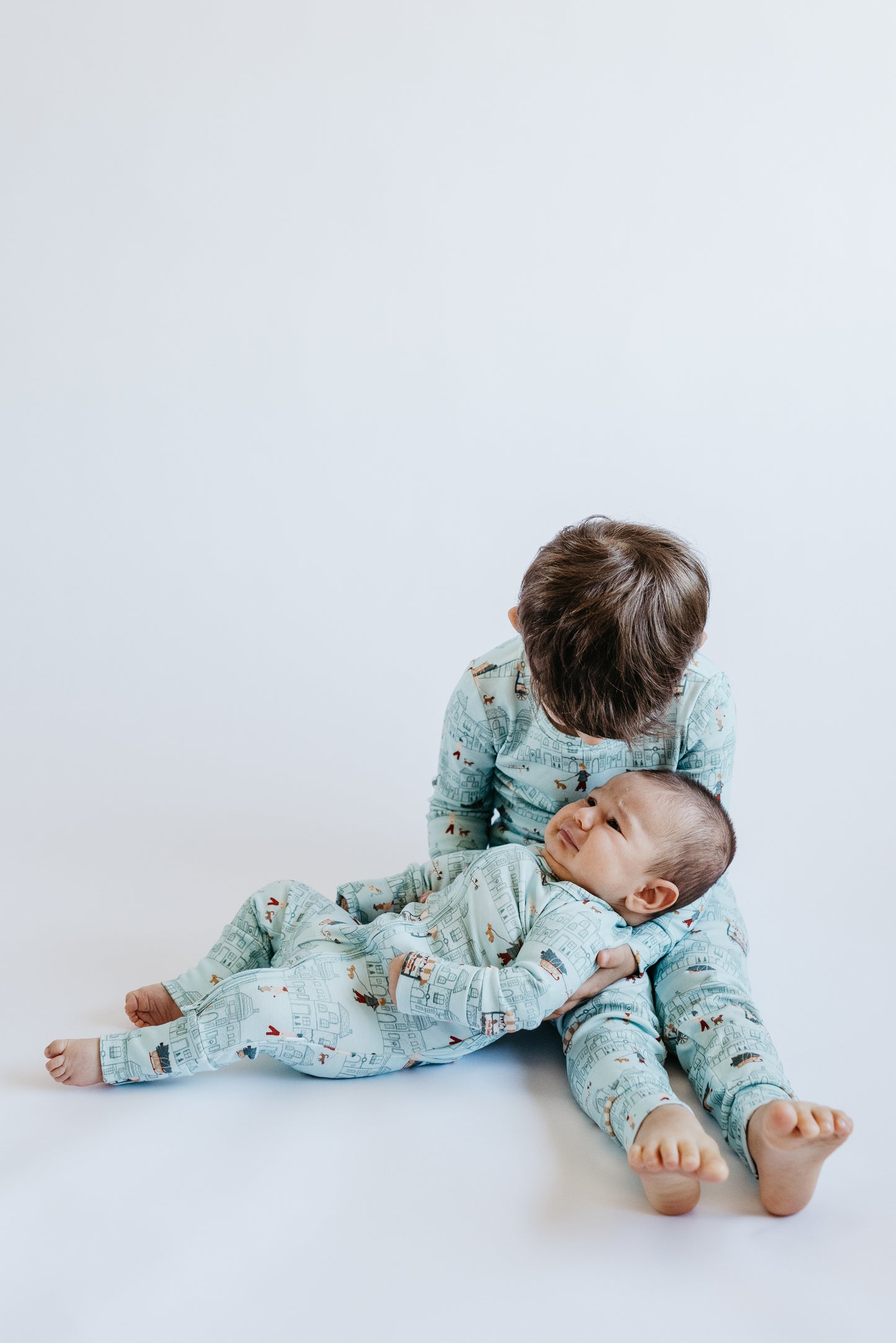 Matching siblings in LURE Merry Little Street — baby footie + kids two-piece with hot cocoa car detail (lifestyle)